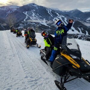 A group of 6 snowmobiles heading up the trail to Paradise with Panorama Mountain resort in the background