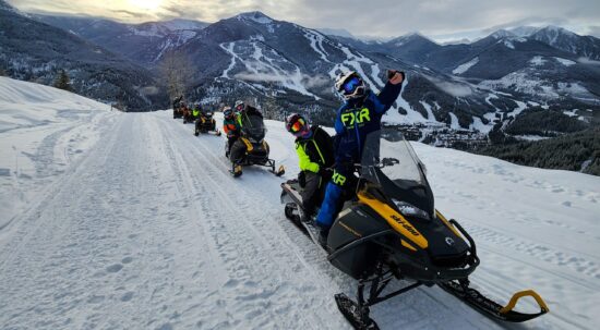 A group of 6 snowmobiles heading up the trail to Paradise with Panorama Mountain resort in the background