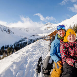Two kids on a snowmobile in front of the Paradise alpine cabin