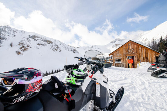 Rider coming out of the alpine Paradise Cabin with a snowmobile in the foreground at Toby Creek Adventures