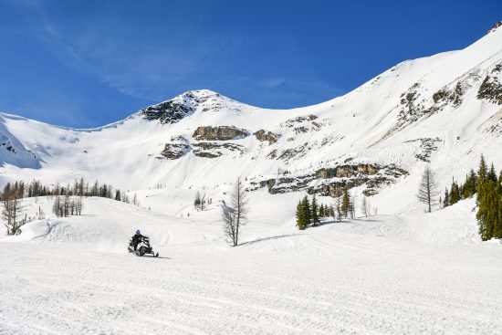 Lone snowmobiler looking small in the beautiful alpine Paradise Basin riding area of Toby Creek Adventures on a sunny day