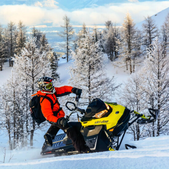 Snowmobiler carving a powder turn while standing on a performance mountain machine during a Powder X tour at Toby Creek Adventures