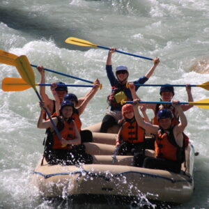 A River Rafting Group with their arms/paddles raised in enjoyment as they raft the Toby Creek with Kootenay River Runners