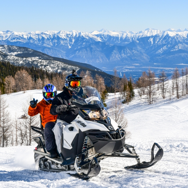 Two riders on a snowmobile having fun with the Rocky Mountain in the background at Toby Creek Adventures