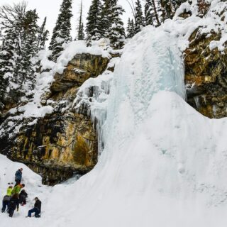 A large Frozen waterfall at Toby Creek Adventures with a group of guests looking at it from below